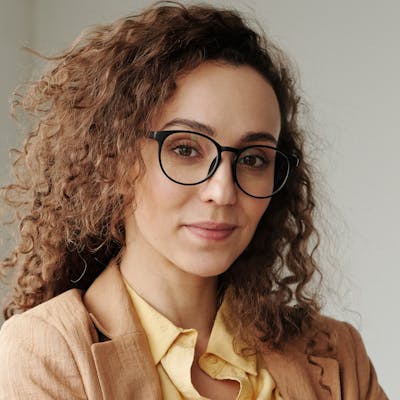 Portrait of a woman with curly hair and glasses in a tan blazer