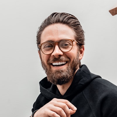 Portrait of a smiling bearded man with glasses in a black hoodie